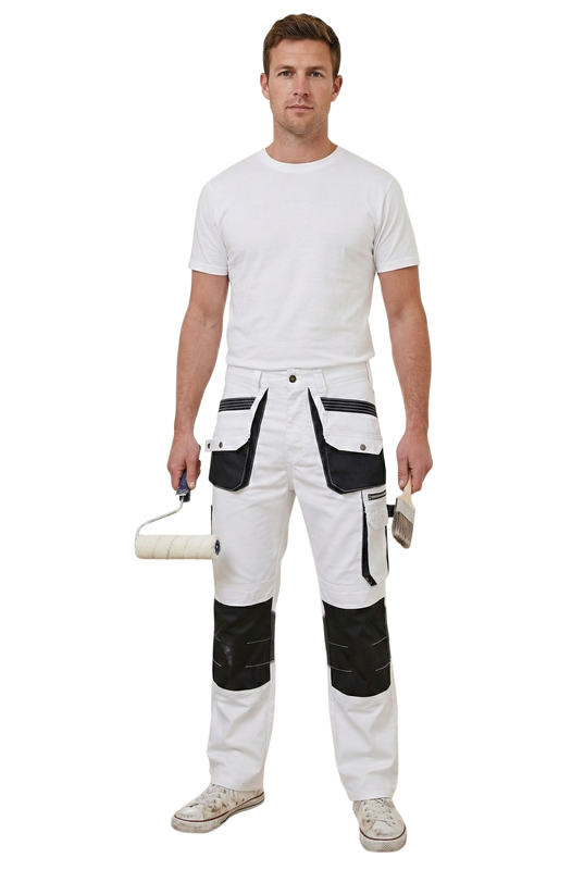 Man wearing white painter work pants with black knee pads and a white shirt, holding a paint roller and brush.